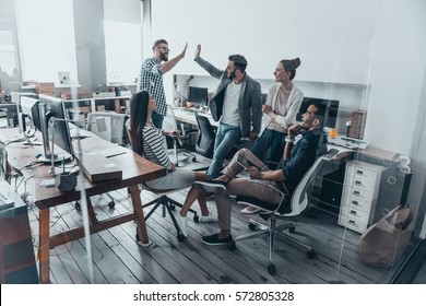 High-five for success! Two cheerful young business people giving high-five while their colleagues looking at them and smiling  - Shutterstock ID 572805328