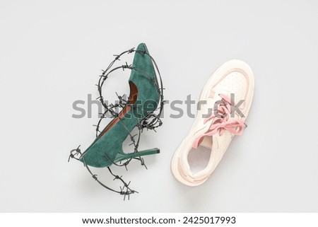High-heeled sneaker and shoe wrapped in barbed wire on white background. Uncomfortable shoes concept
