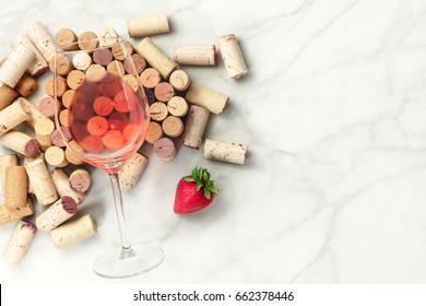 A High-key Overhead Photo Of A Glass Of Rose Wine With Corks And A Fresh Strawberry, On A White Marble Texture With A Place For Text