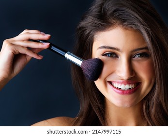 Highlighting Her Best Features. Portrait Of A Gorgeous Young Woman With A Makeup Brush Against A Dark Background.