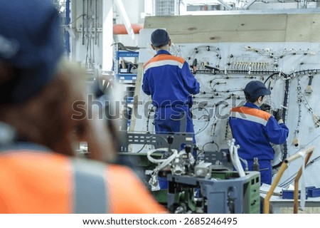 Highlighting precision work. Two technicians meticulously assemble complex wiring harnesses, perfect for electronics, aerospace, manufacturing, and skilled labor themes. Technology and attention to