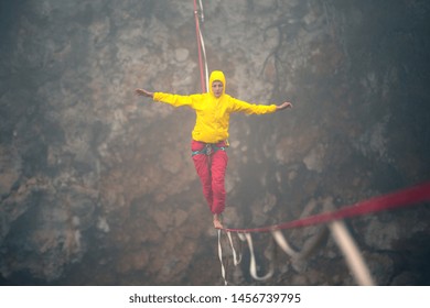 Highline in the fog. Highliner on the background of the rock. A woman catches the balance on a stretched sling. Rope walker in the haze.