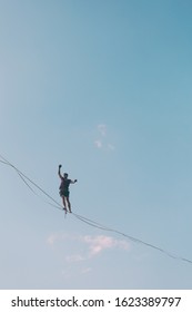Highliner on the background of blue sky makes a move. A man is walking along a stretched sling. Performance tightrope walker. Man balances over the abyss. A decisive step forward. - Shutterstock ID 1623389797