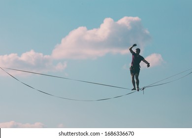 Highliner on the background of blue sky makes a move. A man is walking along a stretched sling. Performance tightrope walker. Man balances over the abyss. A decisive step forward.