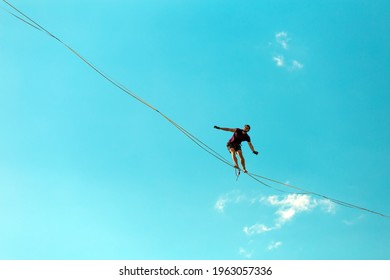 Highliner on the background of blue sky makes a move. A man is walking along a stretched sling view from below. Performance tightrope walker. Man balances over the abyss. A decisive step forward.