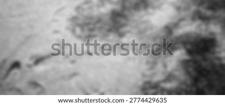 A highly blurred, monochromatic image presenting an abstract texture, possibly suggestive of liquid motion, frosted glass, or ethereal smoke. The lack of sharp focus creates a soft, dreamlike quality with varying shades of gray, inviting interpretation and contemplation.