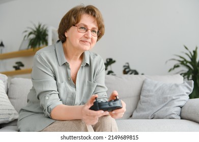 A Highly Emotional Older Lady Sits On The Couch At Home And Plays Video Games. Grandma Wins While Sitting Alone At Home