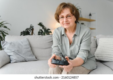 A Highly Emotional Older Lady Sits On The Couch At Home And Plays Video Games. Grandma Wins While Sitting Alone At Home