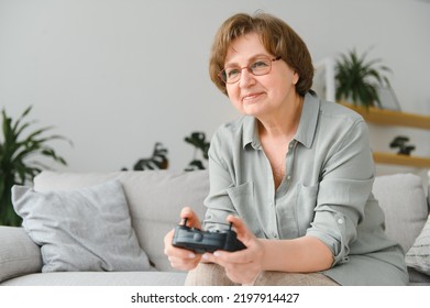 A Highly Emotional Older Lady Sits On The Couch At Home And Plays Video Games. Grandma Wins While Sitting Alone At Home