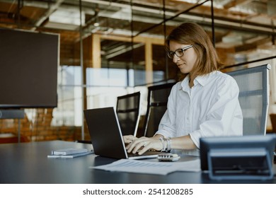 A highly focused businesswoman diligently typing away at her laptop in a stylish and modern office environment - Powered by Shutterstock