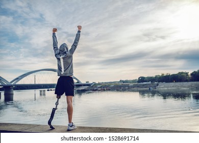 Highly motivated caucasian handicapped sportsman in sportswear and with artificial leg standing on quay and holding arms up. Only way to win is to be yourself. - Shutterstock ID 1528691714