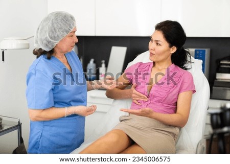 Highly qualified cosmetology doctor working in the clinic tells a young female patient sitting on a couch about the ..health of the female breast, explaining how to properly care for it to maintain a