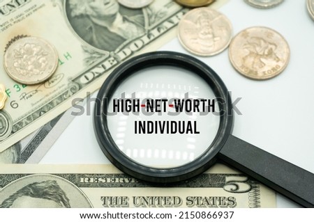 High-Net-Worth Individual.Magnifying glass showing the words.Background of banknotes and coins.basic concepts of finance.Business theme.Financial terms.