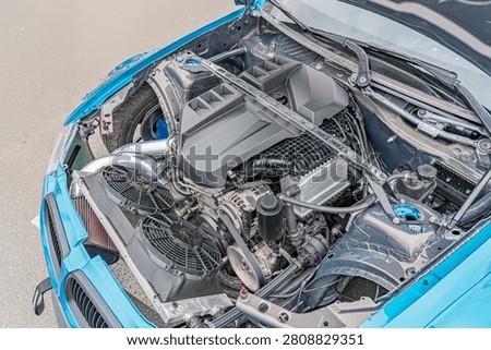 High-performance car engine bay, featuring organized and clean components, including black textured cover, inline-four or inline-six engine, alternator, air intake system, supercharger, air filt.