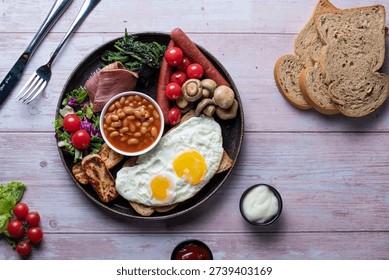 High-quality image of a nutritious breakfast spread featuring fried eggs, crispy bacon, baked beans, sautÃ©ed mushrooms, wholemeal toast, and fresh greens on a rustic wooden table.