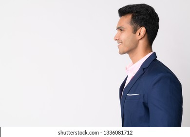 A high-quality studio profile portrait featuring a handsome young Indian or South Asian man in a sharp navy blue suit, smiling while looking off-camera towards the left. The scene is captured against a clean, solid white background that provides a minimalist aesthetic and expansive copy space on the left side of the frame, making the image a perfect choice for graphic designers, digital marketers, and art directors who need to overlay text, promotional headlines, or brand logos. This man features a well-groomed appearance with short, neatly styled dark hair and a clean-shaven face, projecting an image of modern competence, reliability, and approachability. Dressed in a tailored blue blazer over a light pink dress shirt, the model embodies a contemporary, sophisticated look suitable for a variety of corporate or lifestyle contexts. This relaxed side-view posture and positive facial expression communicate a sense of optimism, success, and openness, making the stock photo exceptionally well-suited for a wide range of commercial and editorial uses. These include team profile pages, networking portfolios, recruitment advertisements, and financial or educational marketing materials focused on leadership and human connection. Soft and even lighting highlights the subject's friendly features and creates a welcoming atmosphere. Whether utilized for a tech startup gallery, a blog post regarding workplace culture, or a marketing campaign for a modern service-based business, this versatile portrait captures an authentic and relatable human moment. The subject represents a demographic that fits seamlessly into global marketing campaigns prioritizing inclusivity and trustworthy representation. This shot captures the essence of a modern individual who balances capability with a kind demeanor, making the picture a robust visual asset for any brand seeking to connect with a target audience through high-end photography that stands out in a crowded marketplace. The composition is ideal for website headers, banners, and print media.