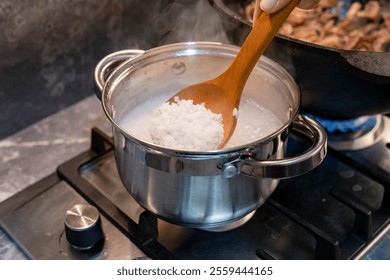  A high-quality, top-view shot capturing the process of cooking rice in an aluminum saucepan on a gas stove. The image shows grains of white rice simmering in boiling water, representing a fundamental step in preparing Asian cuisine, traditional risotto, or a healthy side dish. This authentic 