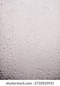 A high-resolution, abstract background image featuring numerous water drops and condensation droplets clinging to a glass surface or windowpane. The drops vary in size