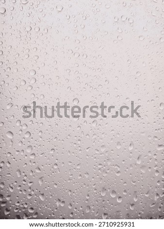 A high-resolution, abstract background image featuring numerous water drops and condensation droplets clinging to a glass surface or windowpane. The drops vary in size