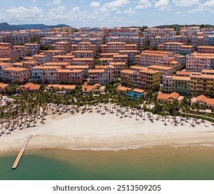 High-resolution aerial view of a modern beachside resort town with beautiful terracotta roofs, green spaces, and clear blue water - Powered by Shutterstock