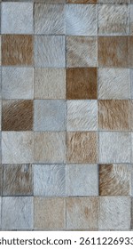High-resolution close-up of a patchwork surface made of natural cowhide or leather squares in varying shades of beige, brown, and grey. Stitched edges and visible hair texture.