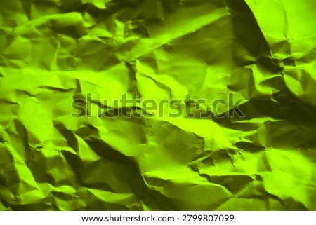 A high-resolution, full-frame background texture of crumpled lime green paper, with complex network of sharp creases, deep folds, and dramatic shadows that create an intense three-dimension.