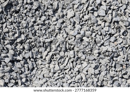 high-resolution, full-frame background texture showing a dense pile of angular, gray crushed stones. The aggregate varies slightly in size and shape, creating a rugged, industrial surface ideal for construction, landscaping, or roadwork design concepts.