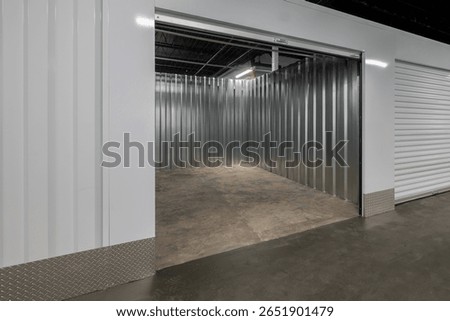 High-resolution image of a clean, empty indoor self-storage unit featuring corrugated metal walls, polished concrete floor, and a partially open roll-up door.