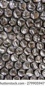 High-resolution macro close-up of black bubble wrap with many popped and deflated bubbles. The crumpled, wrinkled plastic surface creates a unique repetitive pattern with strong light reflections and shadows, giving it a metallic or futuristic look. This damaged packaging material texture conveys concepts of stress, anxiety, protection, fragility, and reuse. Perfect as a background for tech websites, sci-fi designs, mental health content, fidget toy branding, or as a seamless 3D material for industrial and futuristic renderings