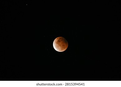 A high-resolution photograph of a partial lunar eclipse featuring a reddish moon illuminated against a dark starry night sky. The image captures the dramatic transition of Earth's shadow across the lunar surface, revealing detailed textures and natural colors. Perfect for astronomy, space science, celestial events, educational materials, lunar calendars, news articles, backgrounds, and creative designs with generous copy space.