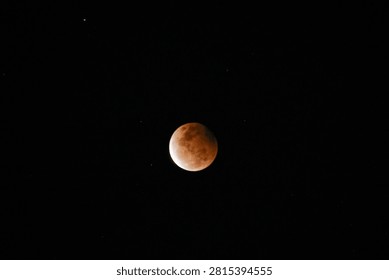 A high-resolution photograph of a partial lunar eclipse featuring a reddish moon illuminated against a dark starry night sky. The image captures the dramatic transition of Earth's shadow across the lunar surface, revealing detailed textures and natural colors. Perfect for astronomy, space science, celestial events, educational materials, lunar calendars, news articles, backgrounds, and creative designs with generous copy space.
