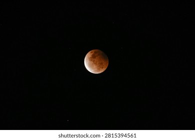 A high-resolution photograph of a partial lunar eclipse featuring a reddish moon illuminated against a dark starry night sky. The image captures the dramatic transition of Earth's shadow across the lunar surface, revealing detailed textures and natural colors. Perfect for astronomy, space science, celestial events, educational materials, lunar calendars, news articles, backgrounds, and creative designs with generous copy space.