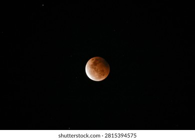 A high-resolution photograph of a partial lunar eclipse featuring a reddish moon illuminated against a dark starry night sky. The image captures the dramatic transition of Earth's shadow across the lunar surface, revealing detailed textures and natural colors. Perfect for astronomy, space science, celestial events, educational materials, lunar calendars, news articles, backgrounds, and creative designs with generous copy space.