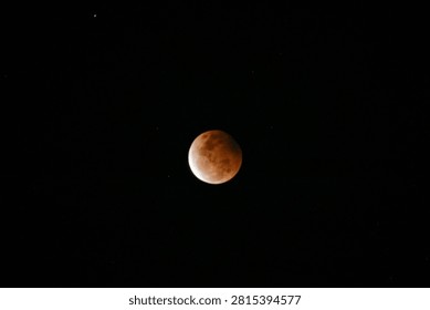 A high-resolution photograph of a partial lunar eclipse featuring a reddish moon illuminated against a dark starry night sky. The image captures the dramatic transition of Earth's shadow across the lunar surface, revealing detailed textures and natural colors. Perfect for astronomy, space science, celestial events, educational materials, lunar calendars, news articles, backgrounds, and creative designs with generous copy space.
