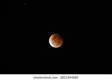 A high-resolution photograph of a partial lunar eclipse featuring a reddish moon illuminated against a dark starry night sky. The image captures the dramatic transition of Earth's shadow across the lunar surface, revealing detailed textures and natural colors. Perfect for astronomy, space science, celestial events, educational materials, lunar calendars, news articles, backgrounds, and creative designs with generous copy space.