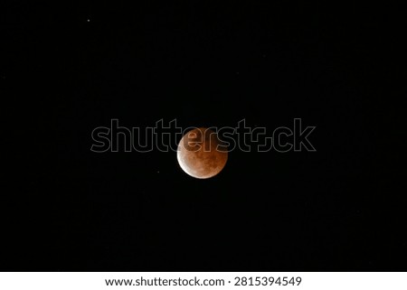 A high-resolution photograph of a partial lunar eclipse featuring a reddish moon illuminated against a dark starry night sky. The image captures the dramatic transition of Earth's shadow across the lunar surface, revealing detailed textures and natural colors. Perfect for astronomy, space science, celestial events, educational materials, lunar calendars, news articles, backgrounds, and creative designs with generous copy space.
