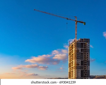 High-rise building, crane, blue sky, white clouds in the light of the setting sun - Powered by Shutterstock