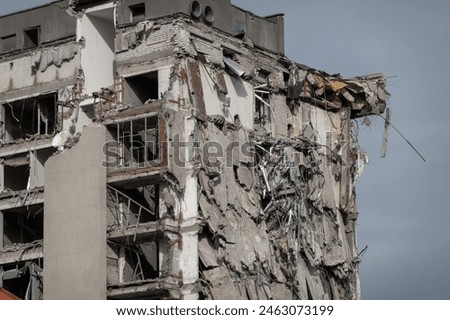 A high-rise building with extensive structural damage, showing exposed brick and debris, likely caused by a disaster. The structure looks unsafe and heavily deteriorated.