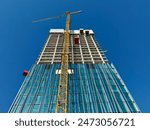 Highrise Building Site. Looking up at the construction site of a high-rise building with yellow crane in the foreground.