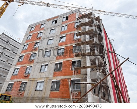 High-rise building under construction with scaffolding and cranes. The facade features exposed bricks and concrete as work continues on the residential project.