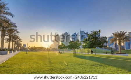 The high-rise district of Doha timelapse at sunset, seen from the Hotel Park, with green lawn and artificial hill in the foreground. Skyscrapers and palms
