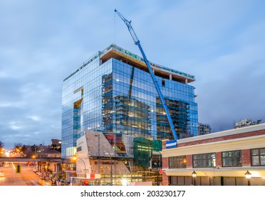 High-rise glass building under construction. The site with crane against evening sky.