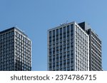 High-rise rectangular paired towers , lined with dark and light panels . Residential building against the blue sky . Modern architecture .
