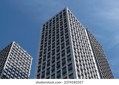 High-rise rectangular paired towers , lined with dark and light panels . Residential building against the blue sky . Modern architecture .