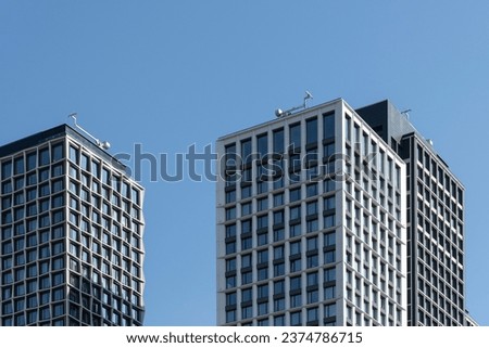 High-rise rectangular paired towers , lined with dark and light panels . Residential building against the blue sky . Modern architecture .