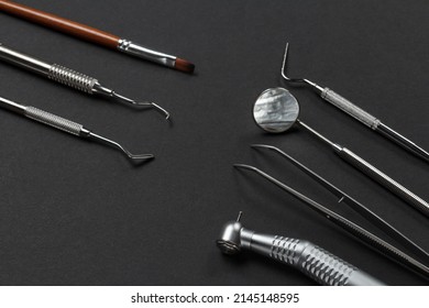 High-speed dental handpiece with bur, tweezers, a mouth mirror and a plugger. Dental restoration instrument, a curette and a brush on the black background. Medical tools. Top view.