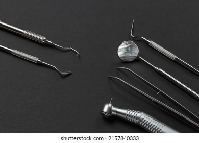 High-speed dental handpiece with bur, tweezers, a mouth mirror and a plugger. Dental restoration instrument and a curette on the black background. Medical tools. Top view.