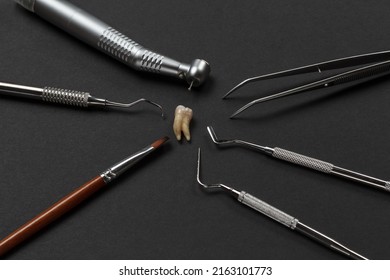 High-speed dental handpiece with bur, tweezers and pluggers. Dental restoration instrument, a curette, a brush and an extracted sick tooth on the black background. Medical tools. Top view.