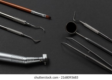 High-speed dental handpiece with bur, tweezers, a mouth mirror and a plugger. Dental restoration instrument, a curette and a brush on the black background. Medical tools. Top view.