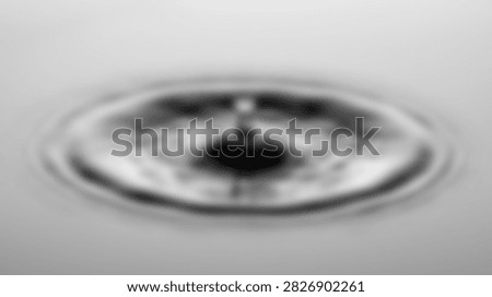 A high-speed macro photograph captures the precise moment a water droplet strikes a liquid surface, generating concentric ripples and splashes.